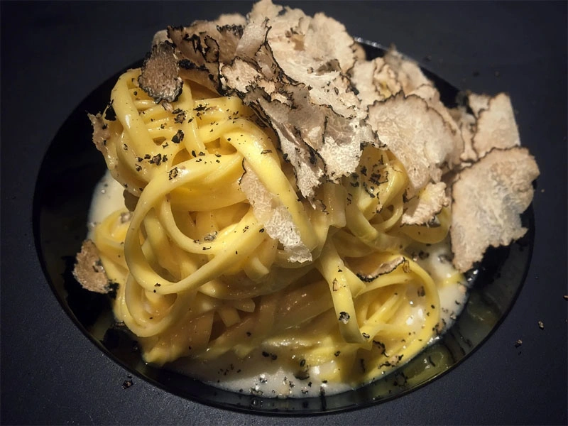 A plate of classic Italian creamy pasta with truffle, elegantly topped with thinly sliced black truffles, showcasing a luxurious and aromatic dish that blends rich, velvety sauce with the earthy flavor of fresh truffles.