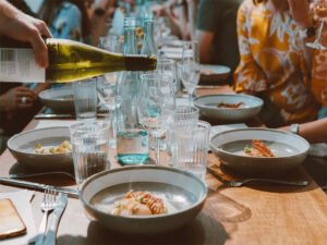A vibrant Italian dinner table set for a festive meal, adorned with colorful dishes wine with pasta and classic ceramics. In the center, a person serves red wine from a traditional bottle, capturing the warmth and conviviality of Italian dining culture